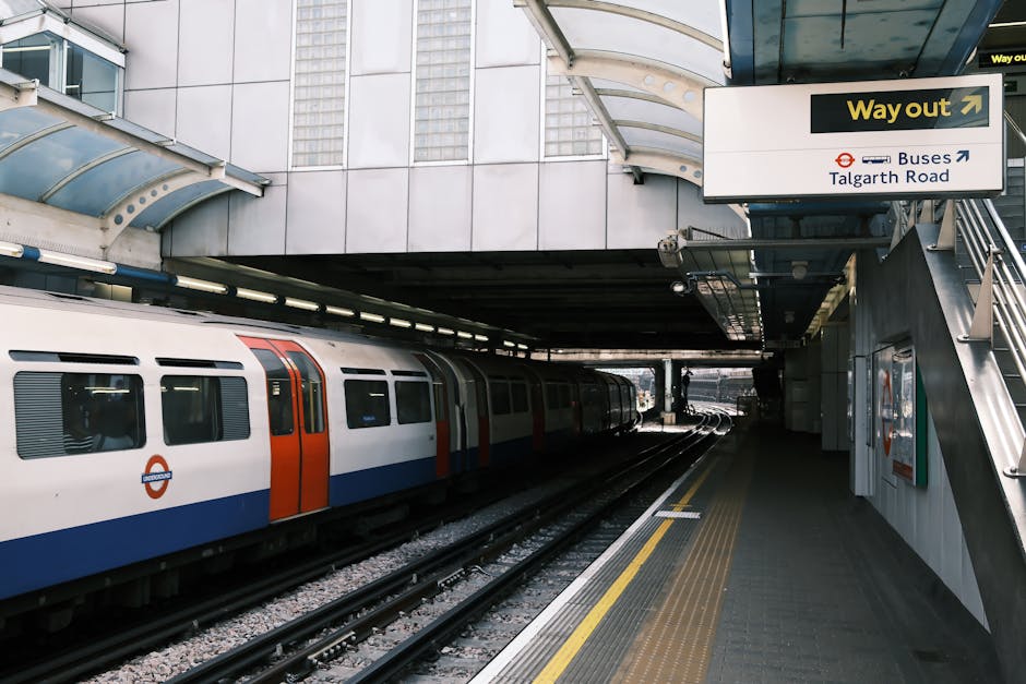 Inside a modern station corridor at Bow Road Station, featuring tiled flooring with a polished, reflective surface, illuminated by natural light from an unseen source. The scene includes a staircase w
